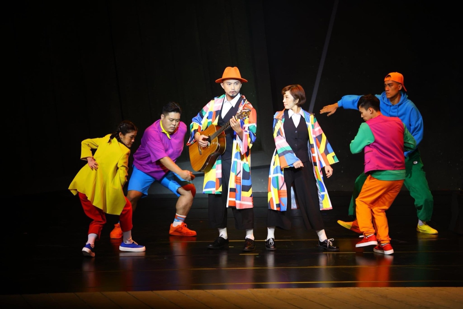 Troubadour in colorful coat with guitar surrounded by performers