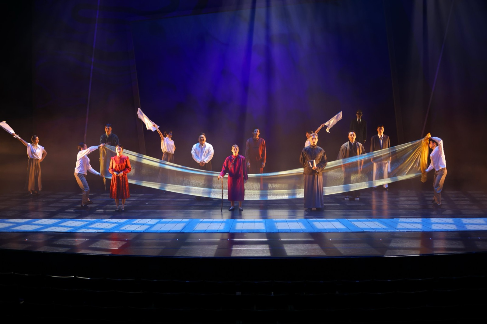 Elder woman with cane and ensemble holding flowing silk fabric in blue light