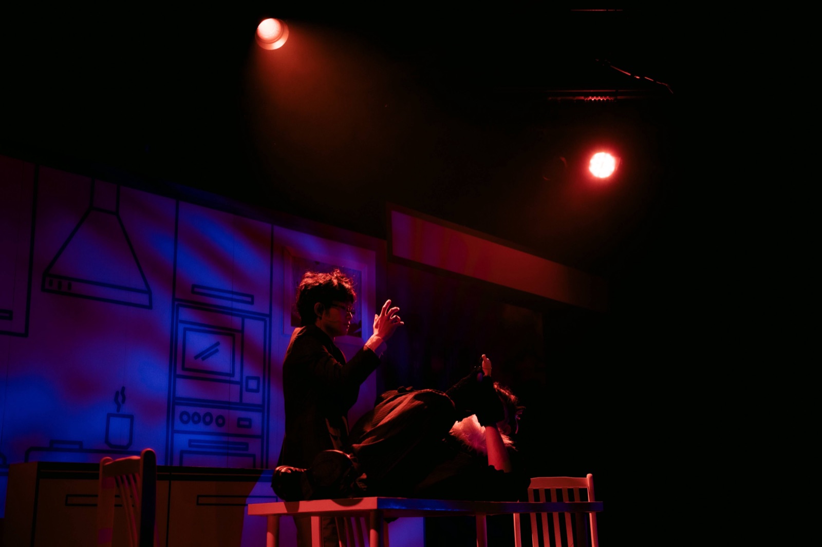Two performers at table in red and blue light