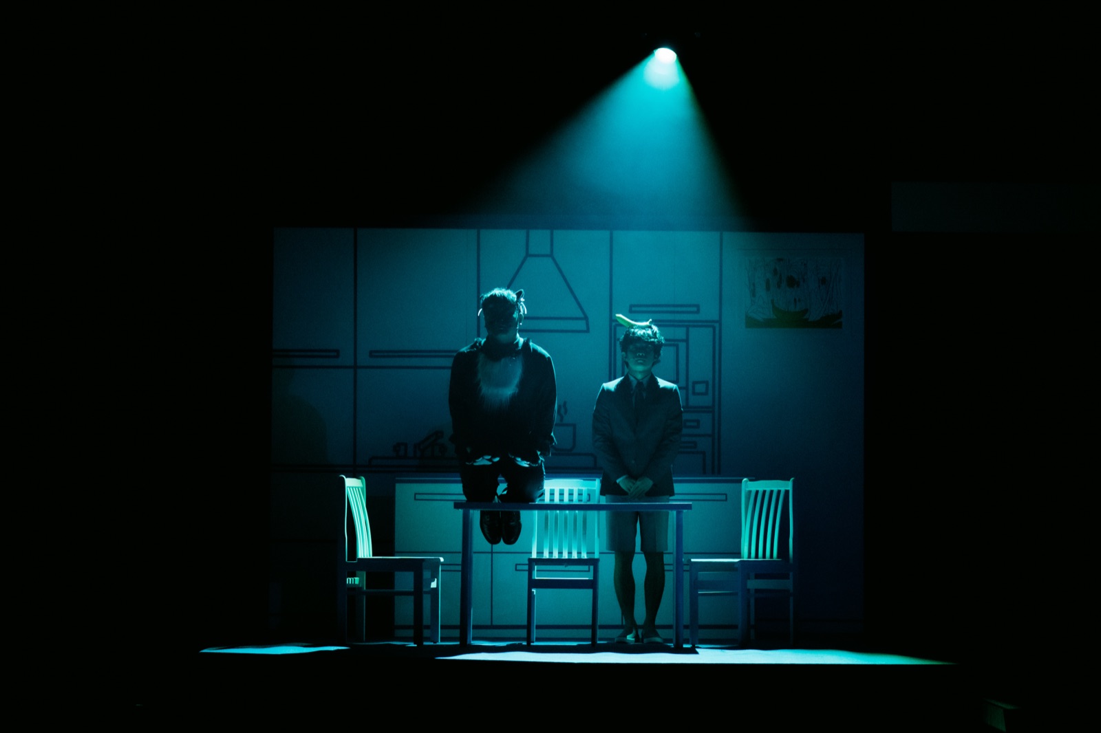 Two figures in teal spotlight with kitchen projection