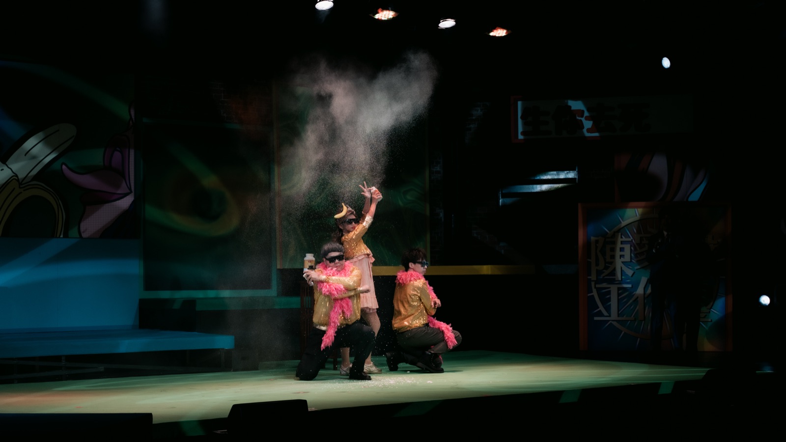 Three performers in gold costumes with powder burst