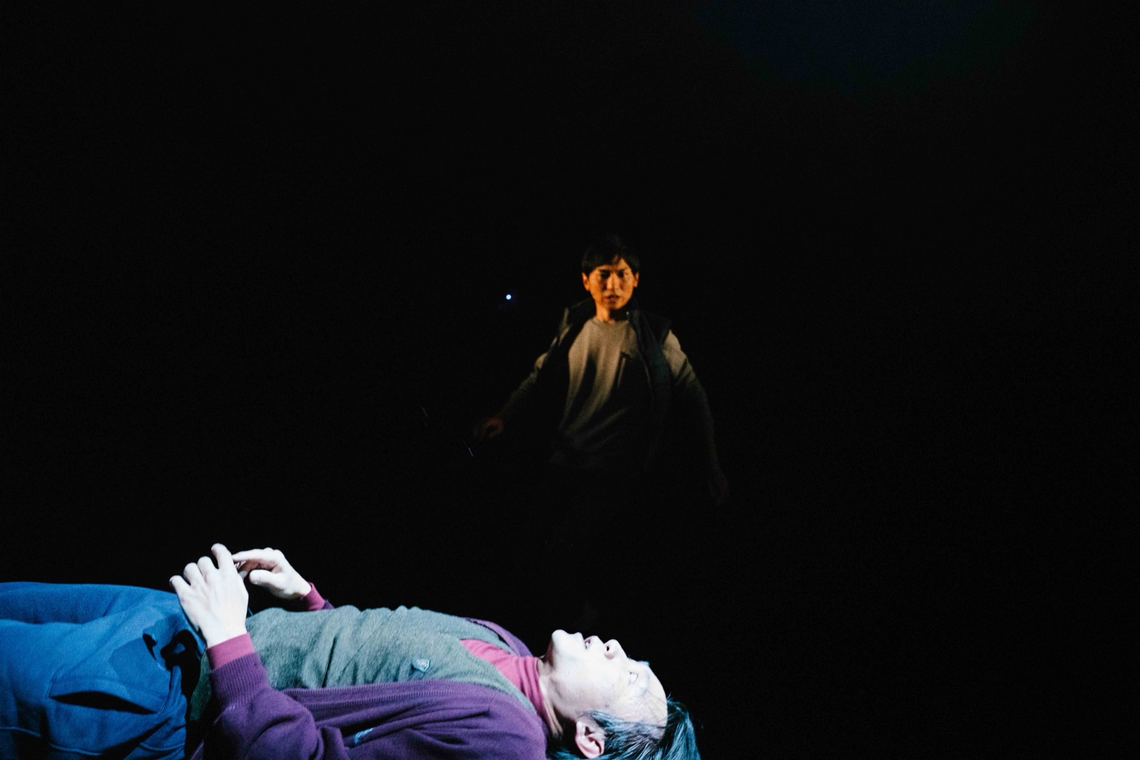 Man lying down with figure watching from behind