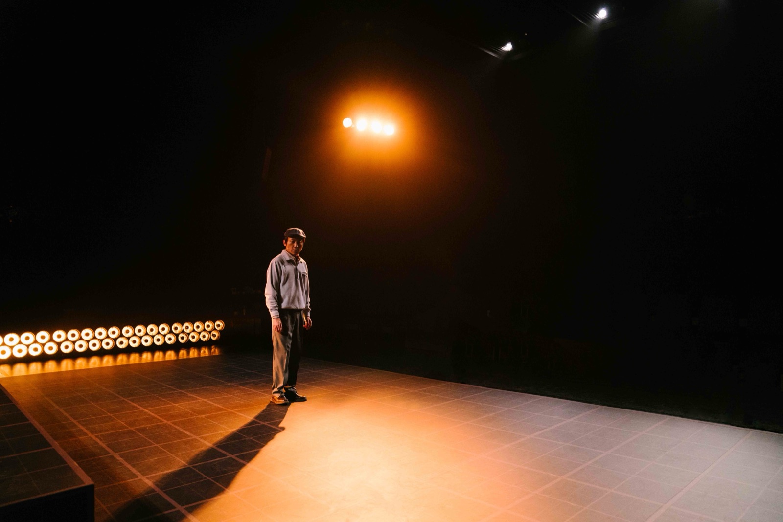 Man on warm-lit stage with row of bulbs
