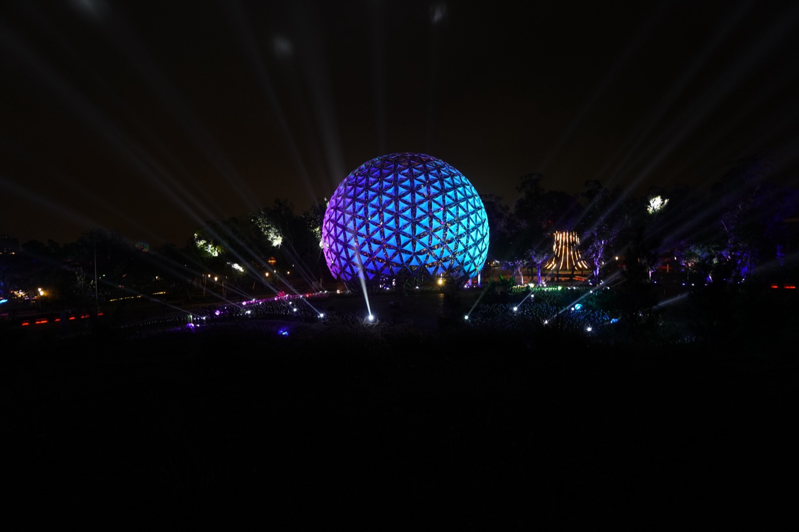 Sphere in blue-purple with beams and illuminated pavilion at night